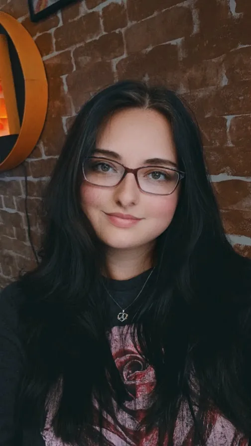 Portrait of Alice wearing glasses in front of a brick wall.