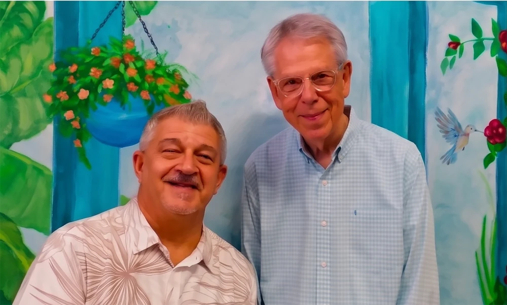Chipper Long and Michael Phillips, co-owners of The Jubilee, standing together in front of a hand-painted mural.