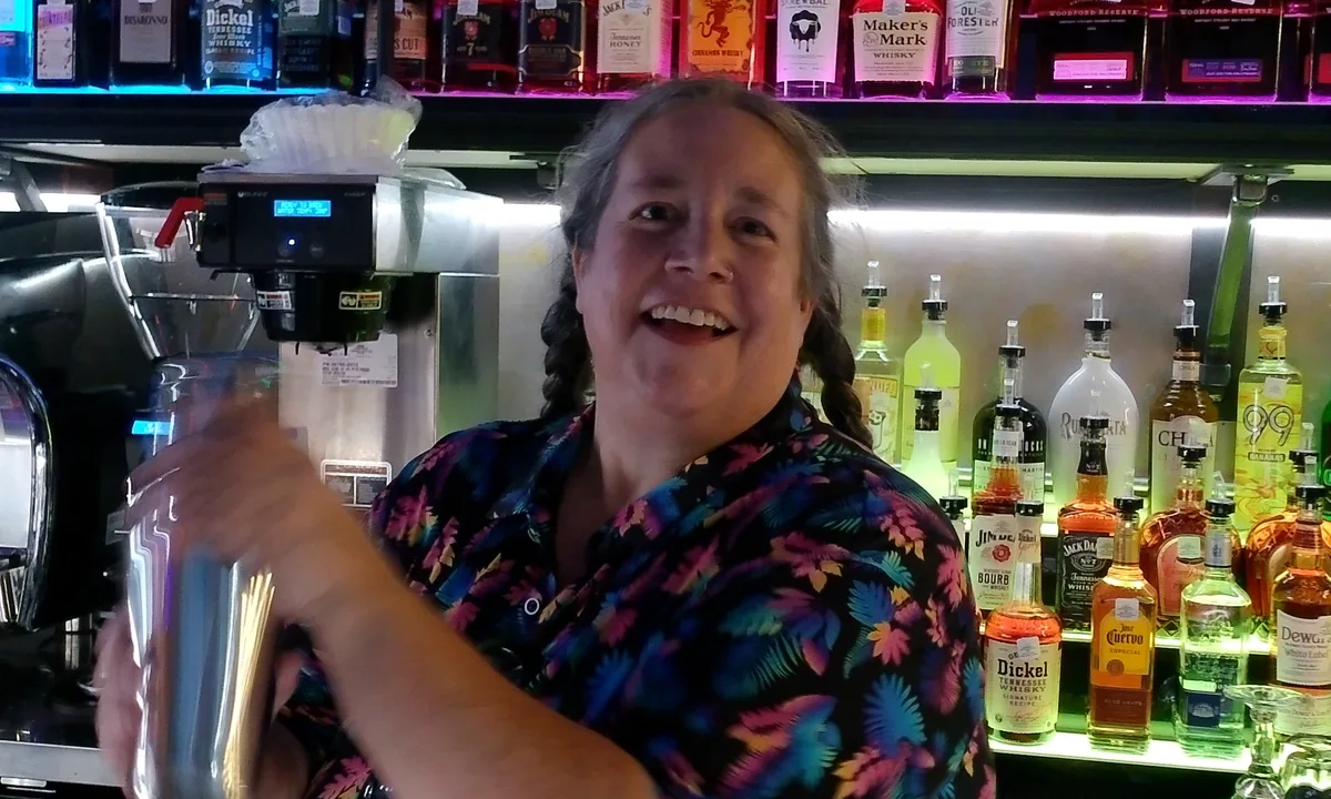 A smiling bartender preparing a drink behind the illuminated Jubilee bar.