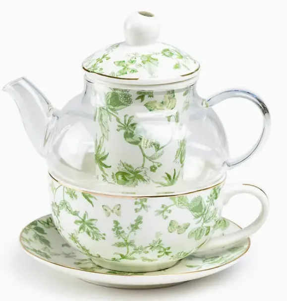 Glass teapot and white cup decorated with trailing green leaves.